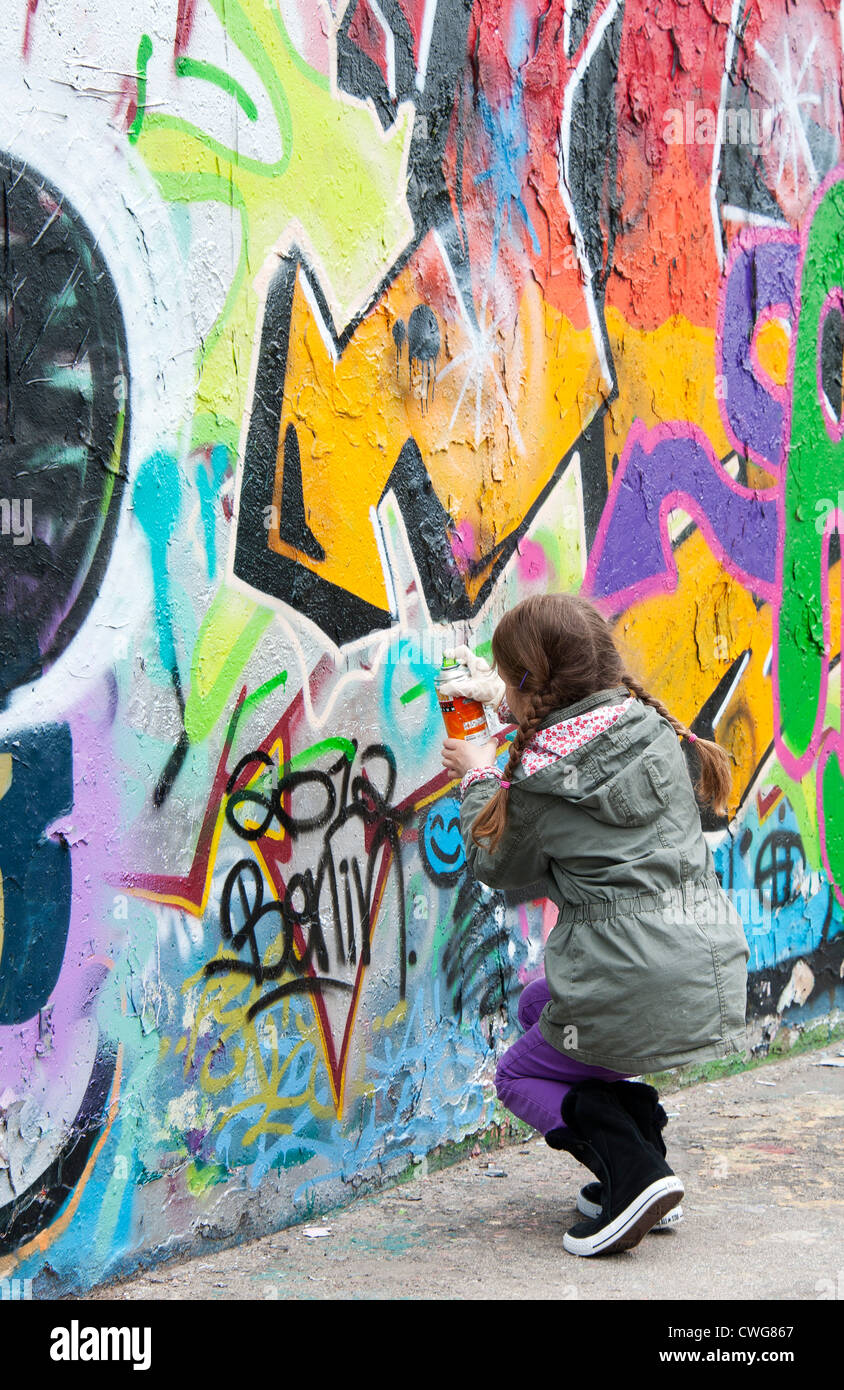 Una giovane ragazza aggiunge il suo segno sulla sommità di altri graffiti su una parte del muro di Berlino, Berlino, Germania. Foto Stock