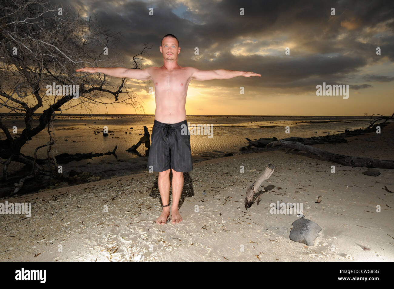 Uomo in posa su una spiaggia con il tramonto del sole Foto Stock