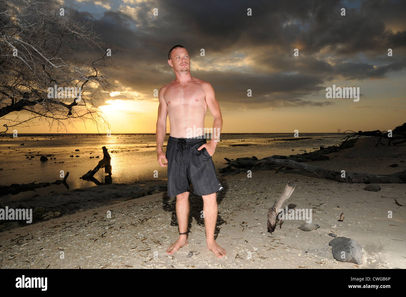 Uomo in posa su una spiaggia con il tramonto del sole Foto Stock