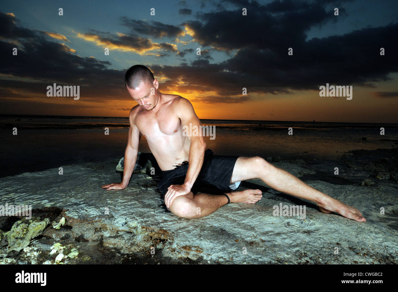 Uomo in posa su una spiaggia con il tramonto del sole Foto Stock