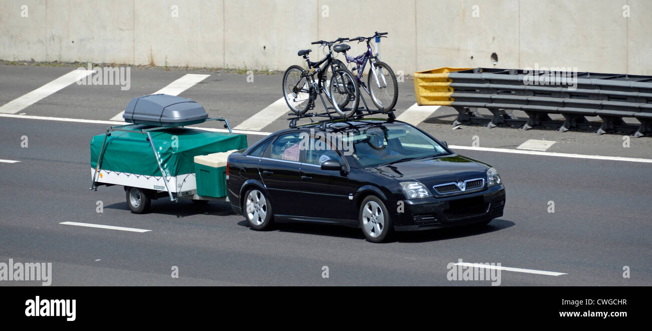 Auto berlina nera a cinque porte con rimorchio pieghevole per camper con copertura e portabagagli sul portapacchi che guida l'autostrada M25 Inghilterra Regno Unito Foto Stock