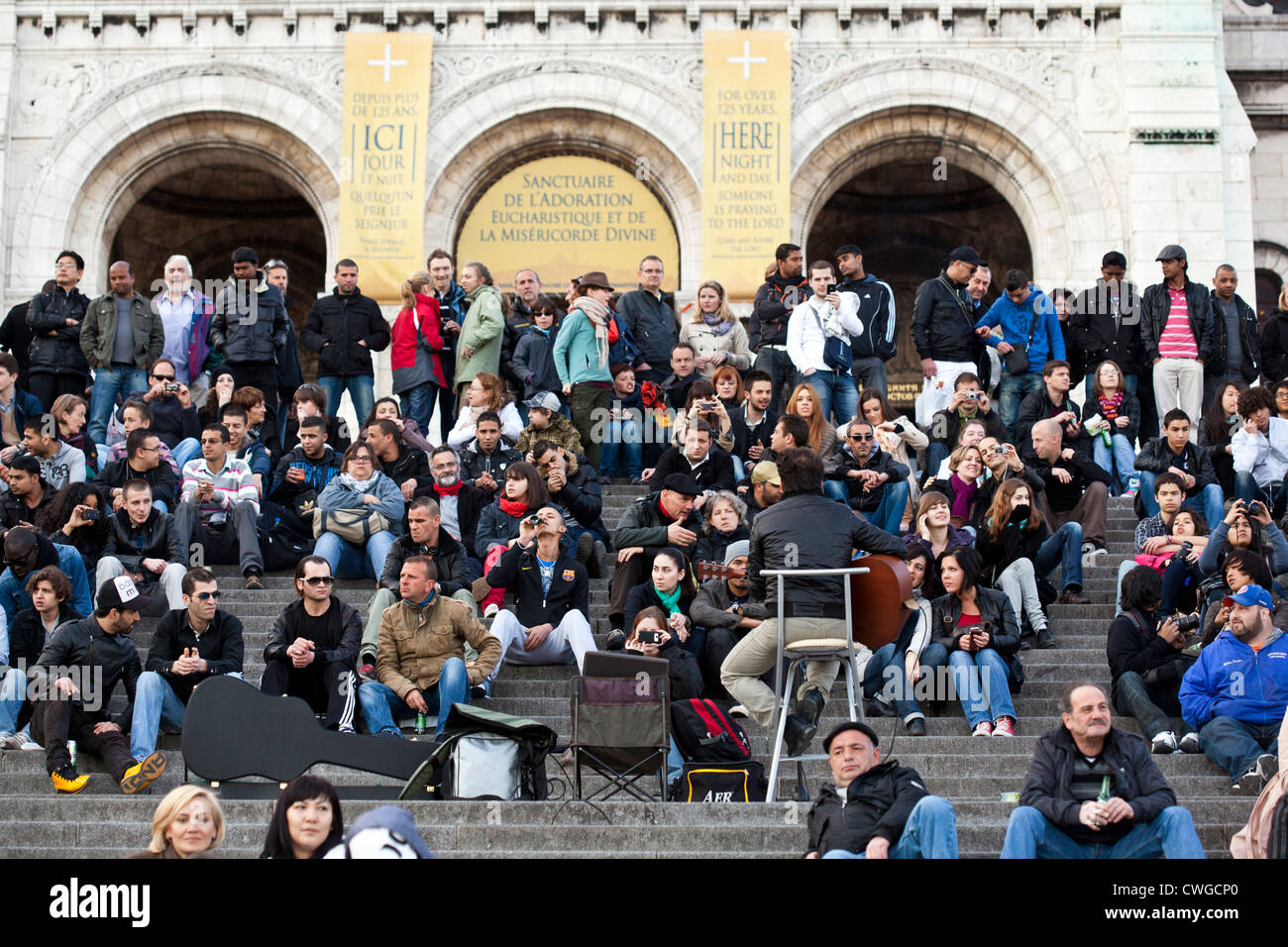 Una folla di turisti per ascoltare un musicista di eseguire sui gradini del Sacre Coeur, Parigi. Foto Stock