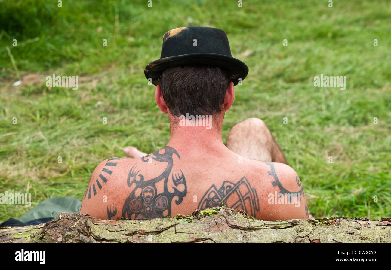 Un gaer del festival gli fa un tatooed indietro mentre distendendosi al festival di musica di Wilderness, Cornbury, Oxfordshire, Regno Unito Foto Stock