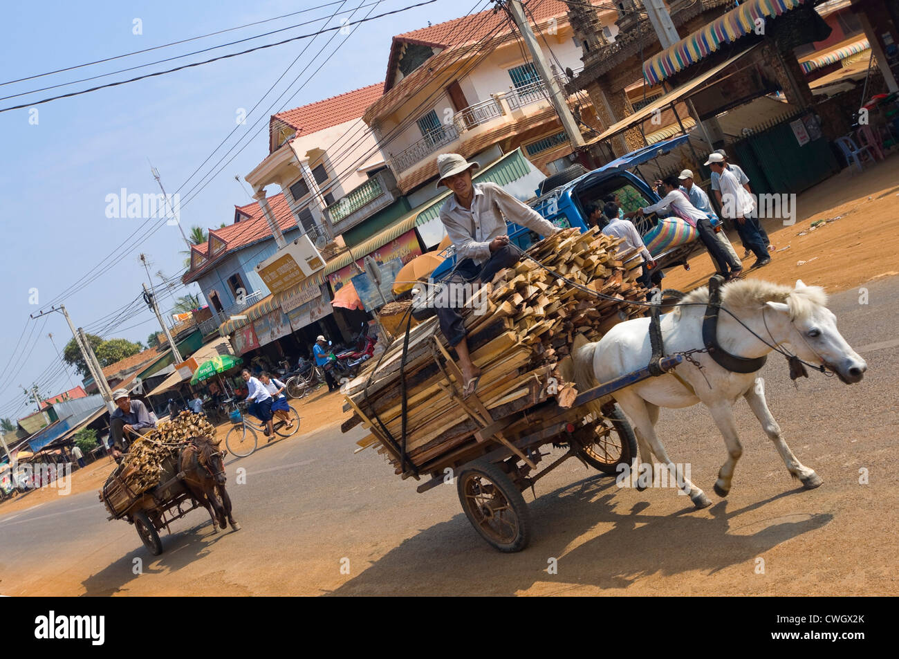 Orizzontale di un ampio angolo di visione di una tipica scena di strada in Cambogia con due lavoratori con i loro pony e carrelli di guida passato. Foto Stock