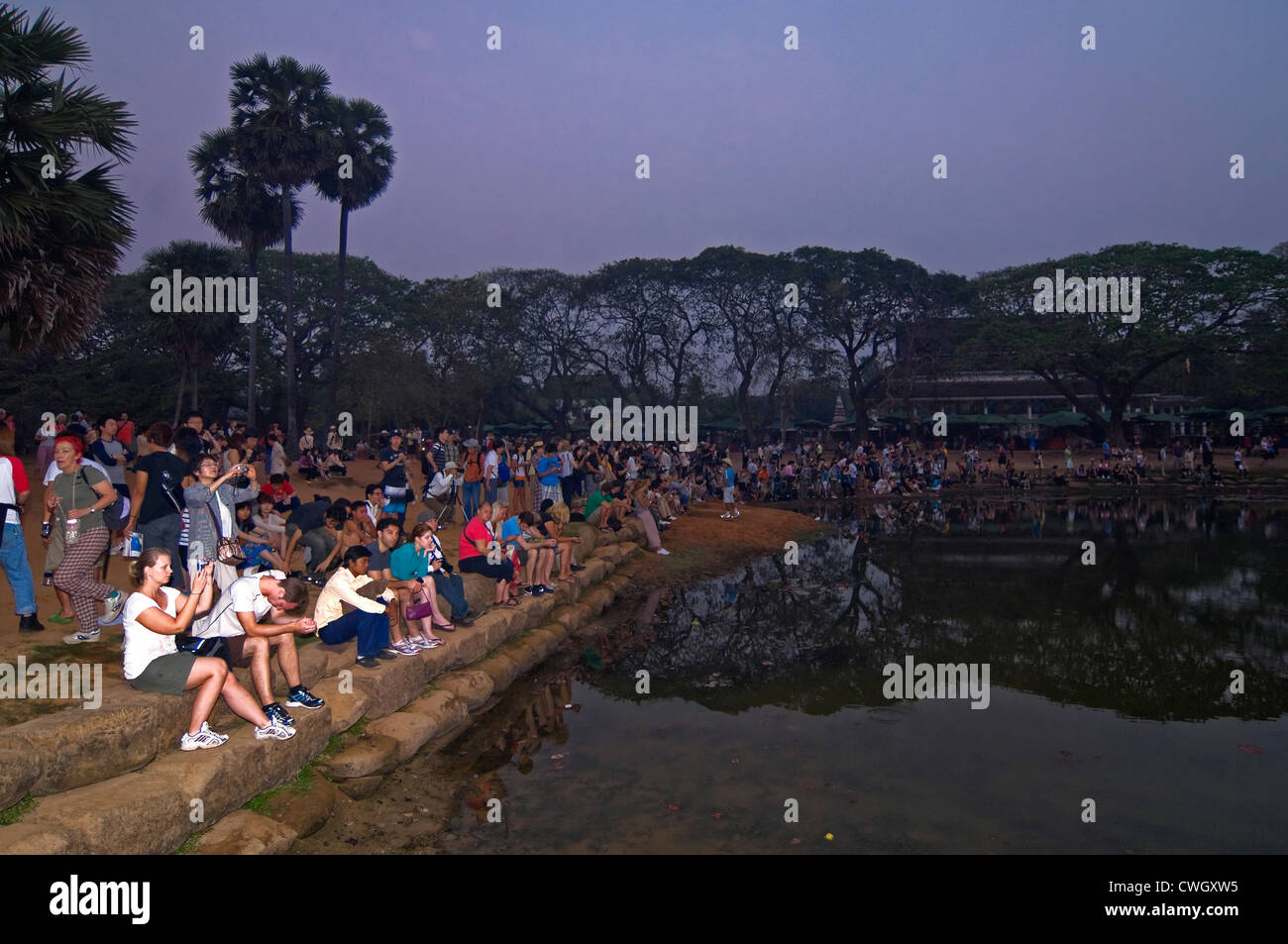 Vista orizzontale di turisti che si siedono insieme intorno ad un lago di guardare il tramonto su Prasat Angkor Wat. Foto Stock