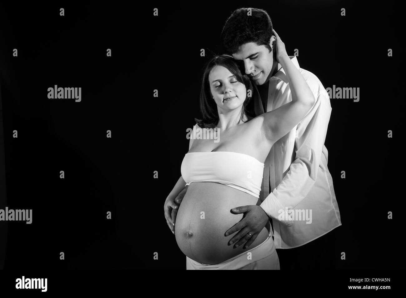 Ritratto in bianco e nero di felice giovane donna incinta essendo abbracciato dal marito. Foto Stock