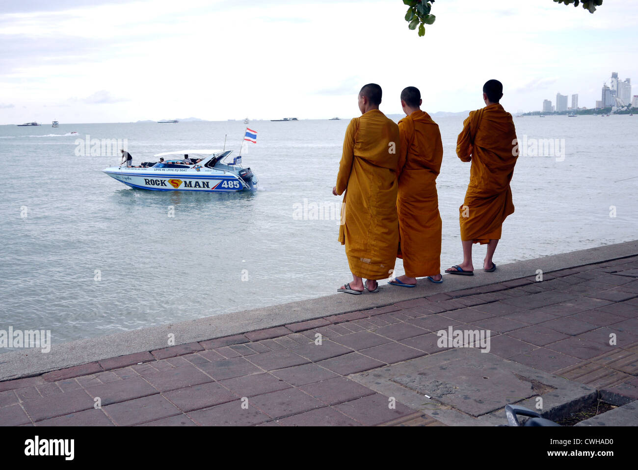 Tre giovani i monaci tailandesi guardando un motoscafo sollevando il dispositivo di ancoraggio per un viaggio in una delle isole locali in Pattaya Thailandia Foto Stock