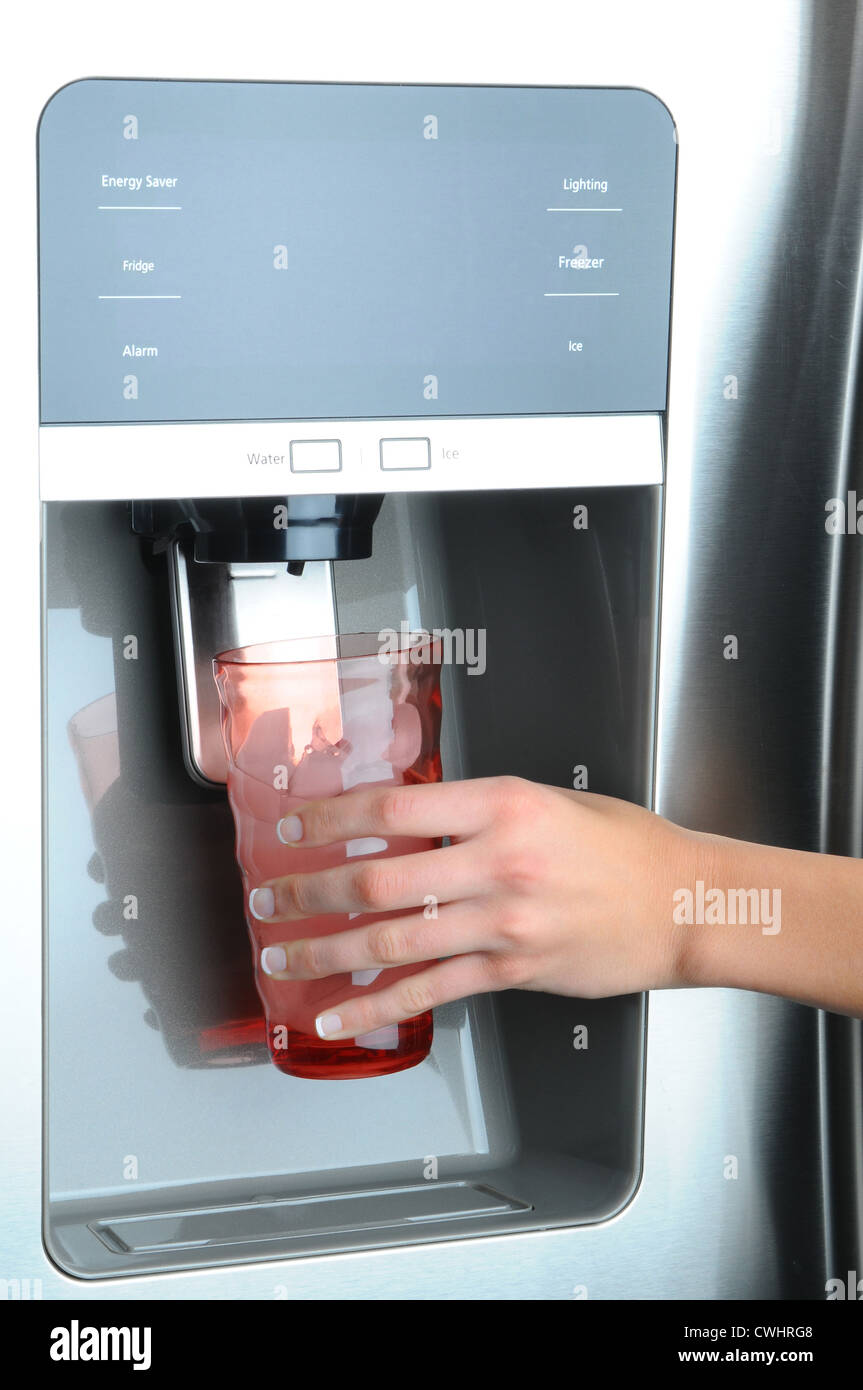 Primo piano di una mano di donna con in mano un bicchiere di acqua e ghiaccio erogatore di un moderno frigorifero Foto Stock