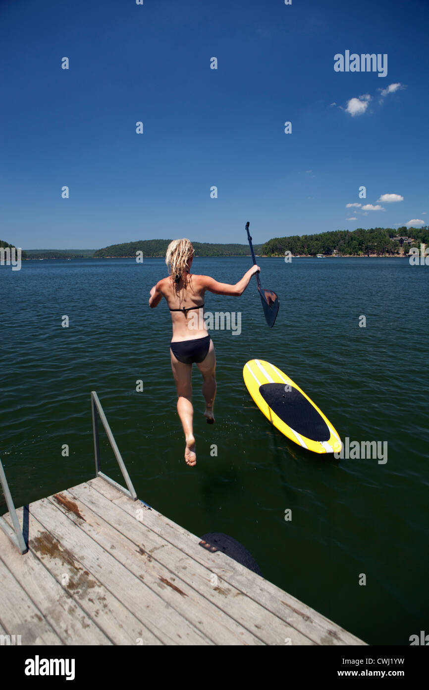 Caucasian donna che si tuffa nel lago accanto a paddleboard Foto Stock