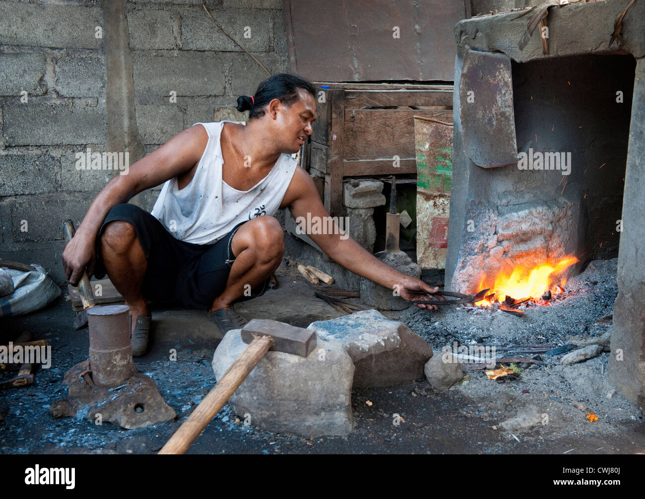 In un fabbro ferraio di villaggio nel centro di Bali, Indonesia, un uomo forges una raccolta degli agricoltori la falce comunemente visto in terrazze di riso. Foto Stock