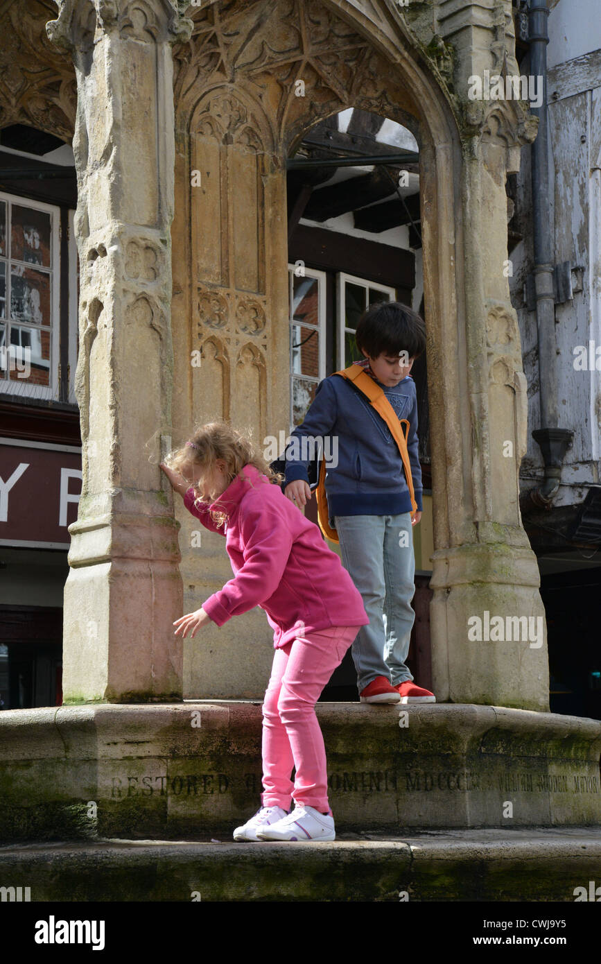 Bambini che giocano sulle fasi del xv secolo alta croce (Buttercross), High Street, Winchester, Hampshire, Inghilterra, Regno Unito Foto Stock