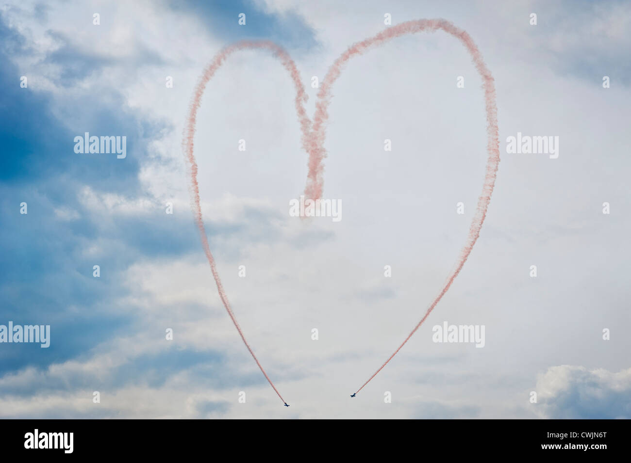 Rosa sentieri di fumo da un acrobazia aerea team display formando un amore cuore simbolo nel cielo. Concetto di immagine Foto Stock