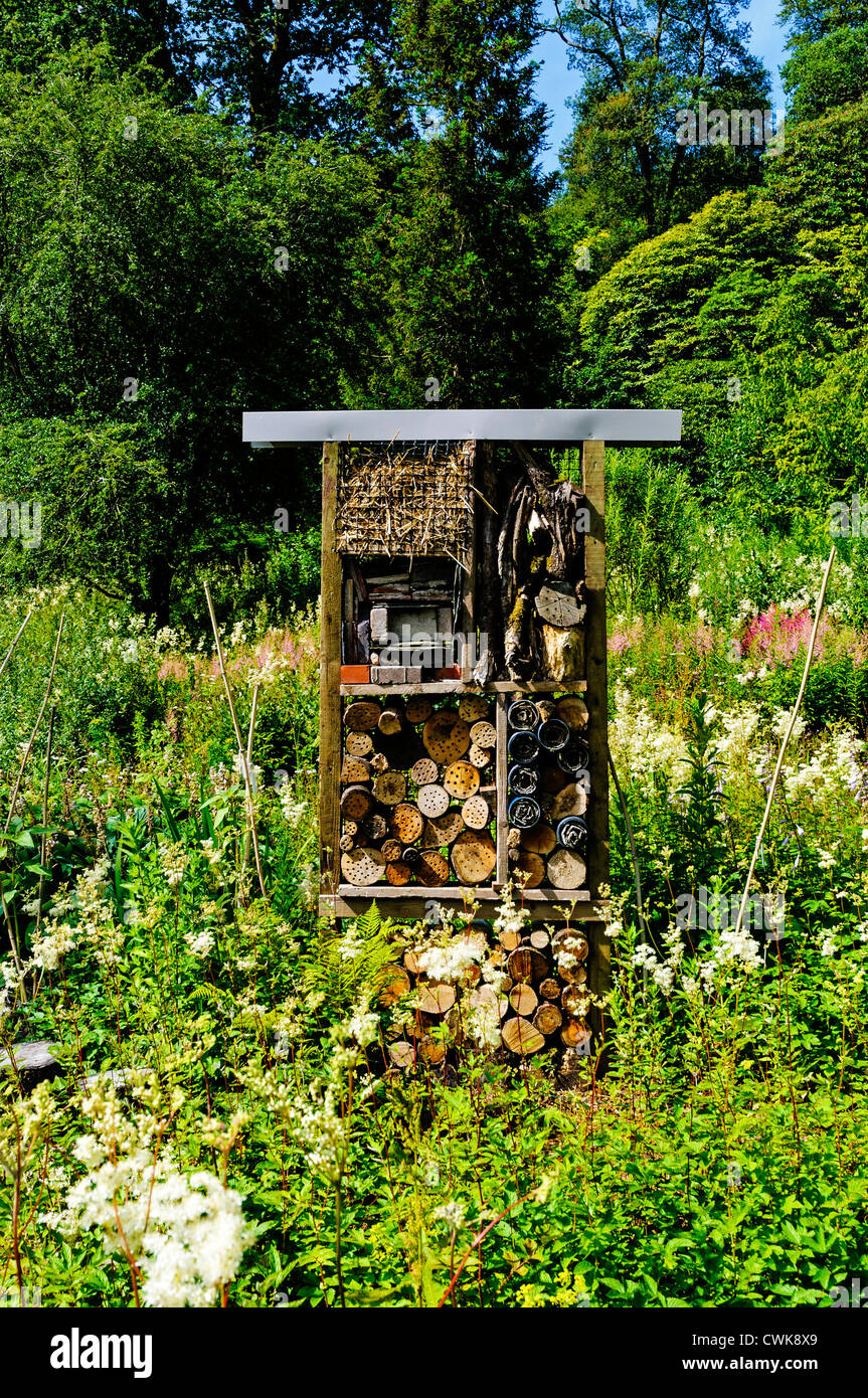 Una struttura di legno insetto casa costruita di paglia, mattoni, registri di corteccia e set di cartone in un giardino naturale pieno di fiori di campo Foto Stock
