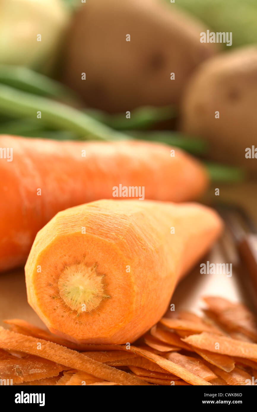 Materie sbucciate la carota con sbucciatore e altri ortaggi o legumi (fagioli verdi e patate) sulla tavola di legno (messa a fuoco selettiva) Foto Stock