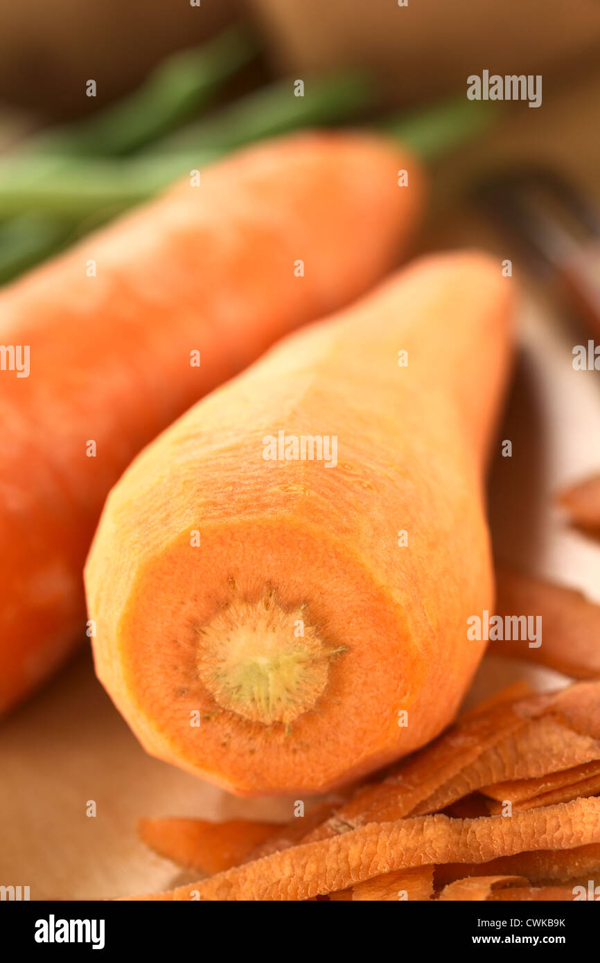 Materie sbucciate la carota con buccia e altri ortaggi o legumi (fagioli verdi e patate) sulla tavola di legno (messa a fuoco selettiva) Foto Stock