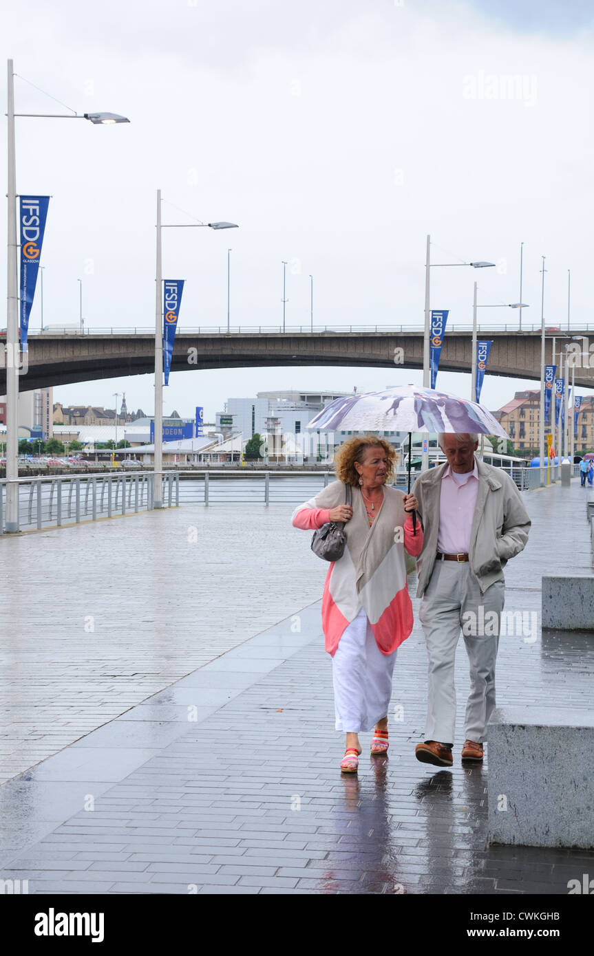 Una coppia matura camminando sotto la pioggia sul lungofiume in Glasgow Foto Stock