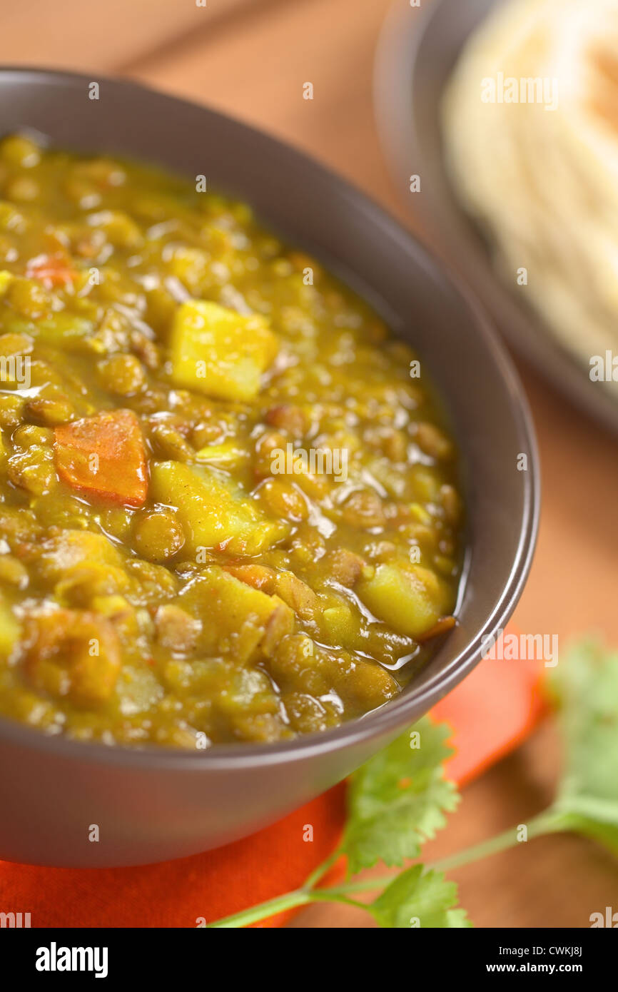 Ciotola di indiano piccante dal (lenticchia) curry preparato con la carota e la patata, chapati flatbread nel retro e foglie di coriandolo Foto Stock