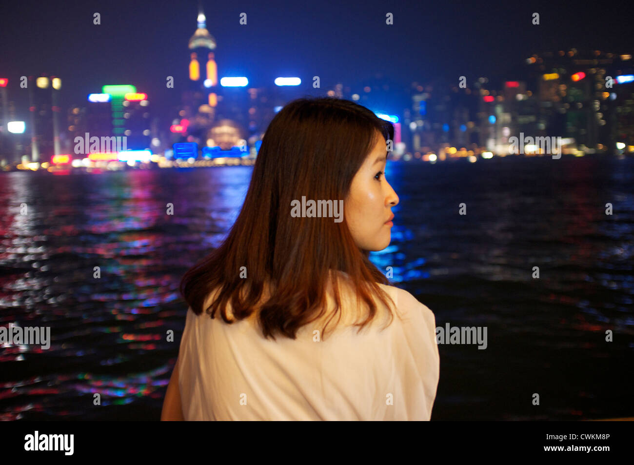 Una ragazza si siede sul lato di Kowloon di Victoria Bay cercando attraverso i grattacieli e il quartiere degli affari di Hong Kong Island. Foto Stock