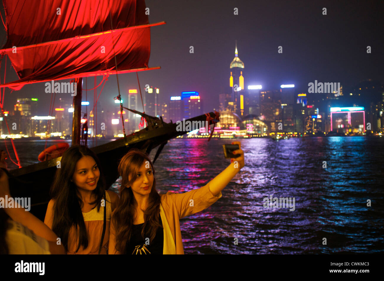 Due ragazze prendere una foto souvenir con un telefono cellulare sul lato di Kowloon di Victoria Bay di Hong Kong. Foto Stock