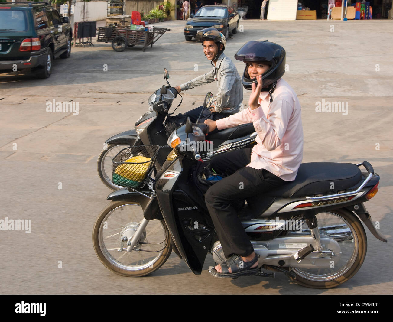 Ritratto orizzontale di due ragazzi in sella ciclomotori fianco a fianco con una strada in discesa in Cambogia. Foto Stock