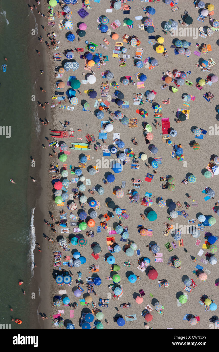 VISTA AEREA VERTICALE. Spiaggia pubblica affollata con ombrelloni colorati nella località balneare di Viareggio. Provincia di Lucca, Toscana, Italia. Foto Stock
