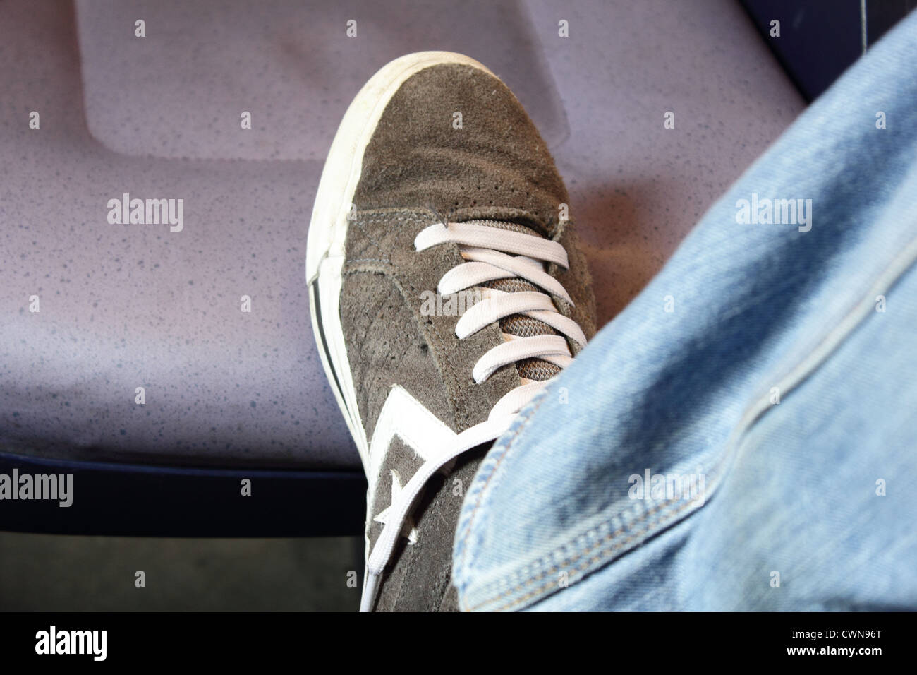 Un piede con Converse mostrano in appoggio sul sedile di un treno Foto Stock