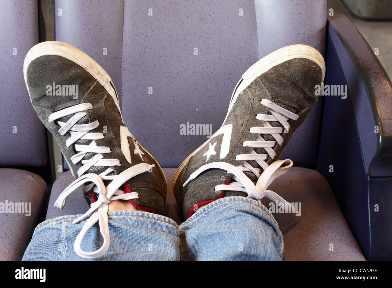 Due piedini con un Converse mostrano in appoggio sul sedile di un treno Foto Stock