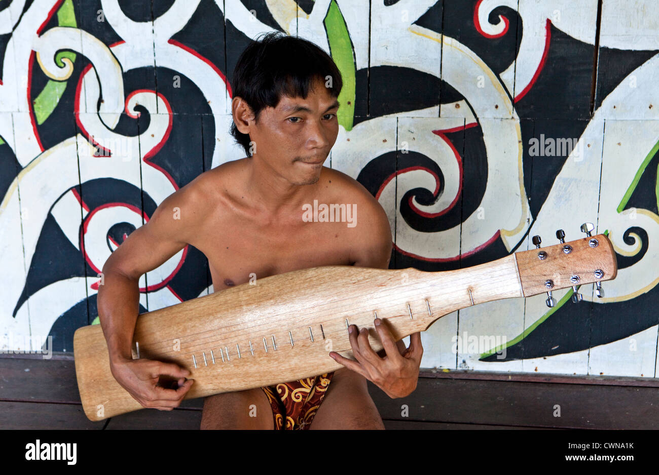 Musicista del Orang Ulu tribù giocando un Sape o Sarawakian chitarra in Longhouse, Sarawak Villaggio Culturale, Kuching, Borneo, Mal Foto Stock