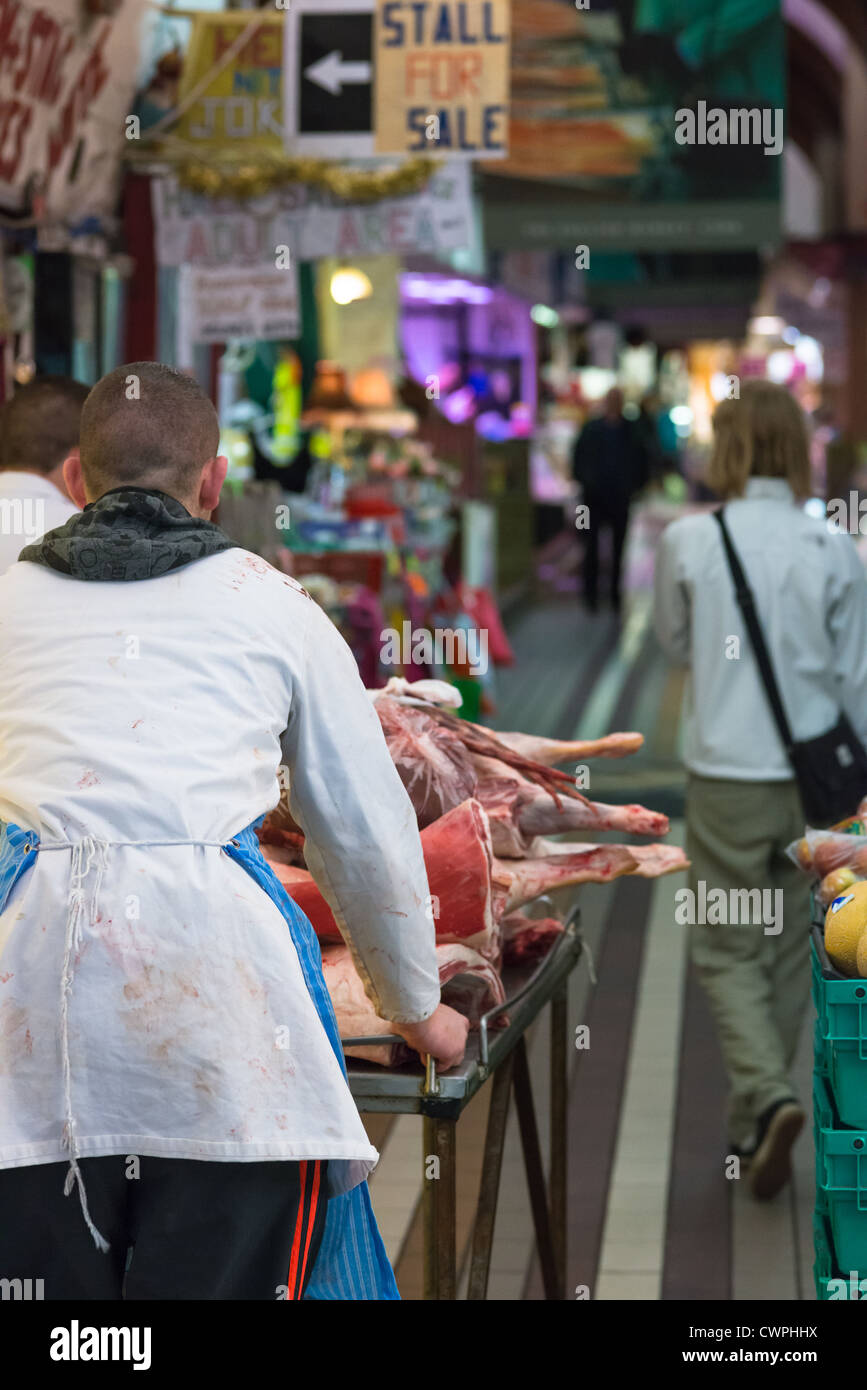 Macelleria assistant portando carni fresche al mercato inglese della città di Cork, Repubblica di Irlanda. Foto Stock