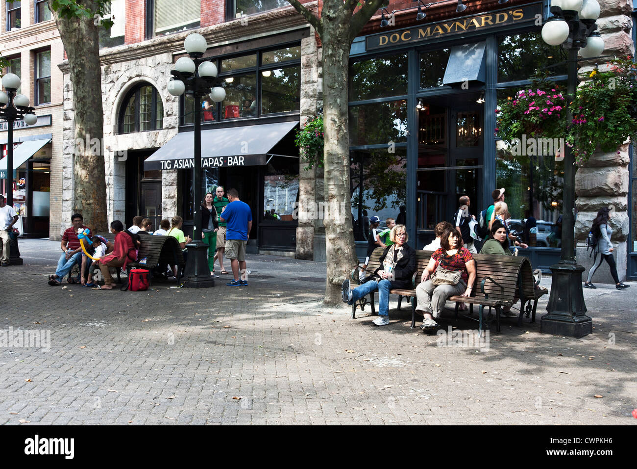 I diversi gruppi di persone godetevi il relax sulle panchine o passeggiando in sun pezzata Pioneer Square centro storico di Seattle Foto Stock