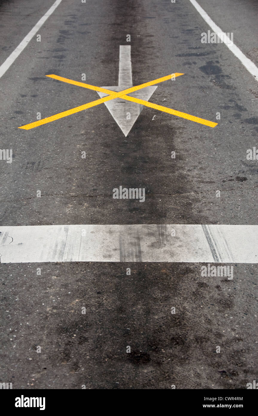 Segno di freccia e altri contrassegni sulla strada asfaltata Foto Stock