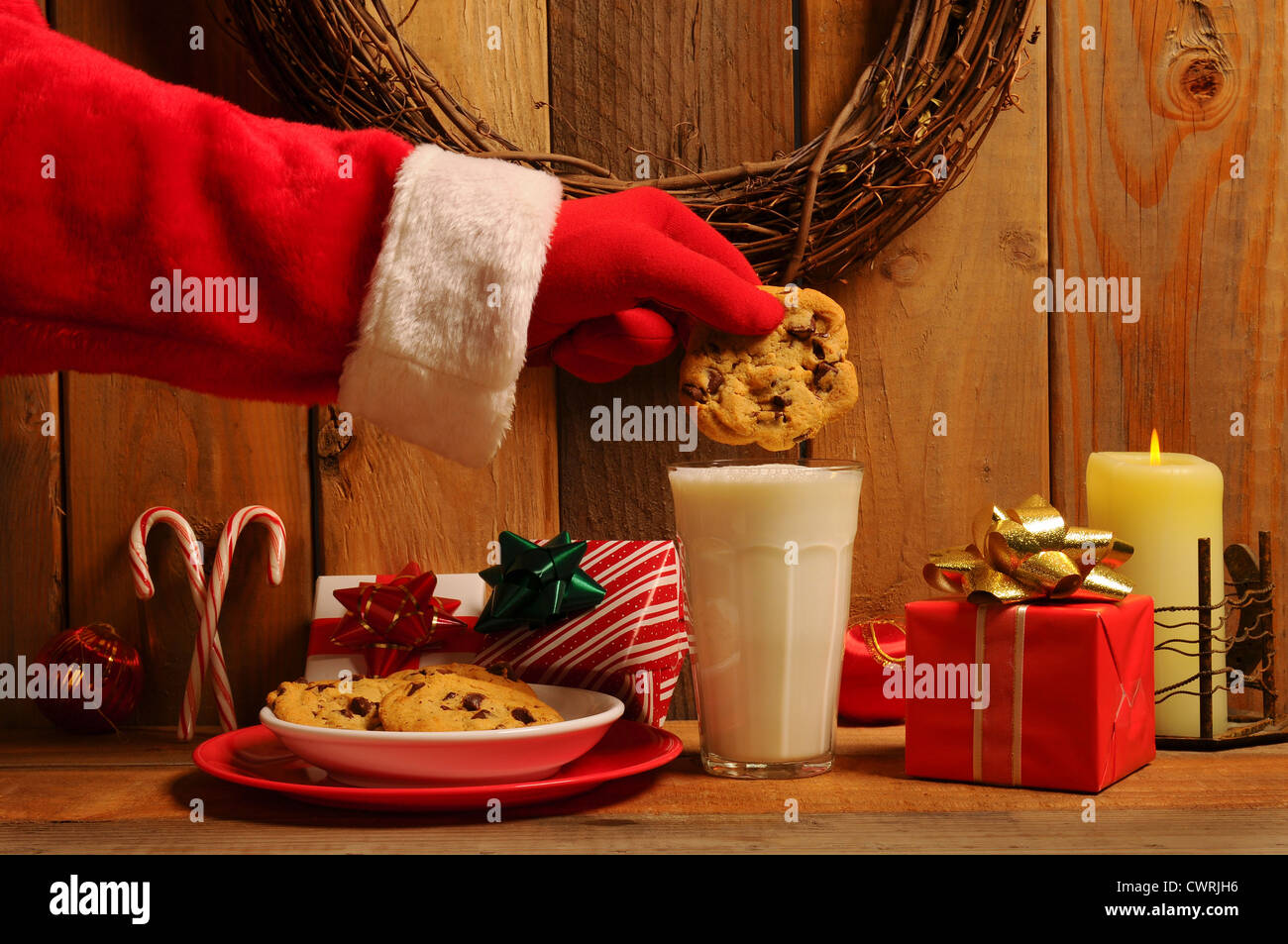 Santa Claus circa di dunk a pezzetti di cioccolato in un bicchiere di latte in un rustico di vecchia impostazione. Foto Stock