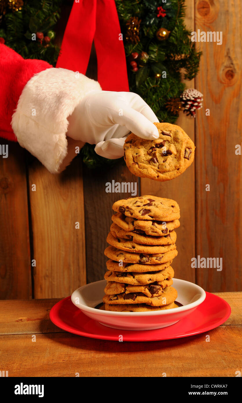 Santa Claus prendendo un Chocolate Chip Cookie dalla pila di grandi dimensioni sulla piastra. Foto Stock