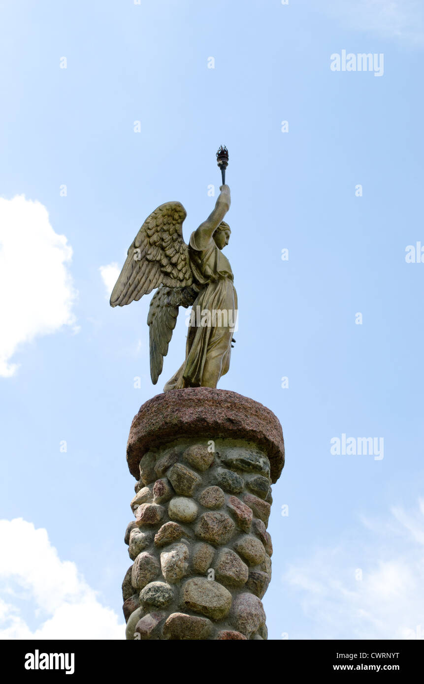Angelo azienda fiaccola su sfondo con cielo nuvoloso. Statua sulla piattaforma fatta di pietre. Foto Stock