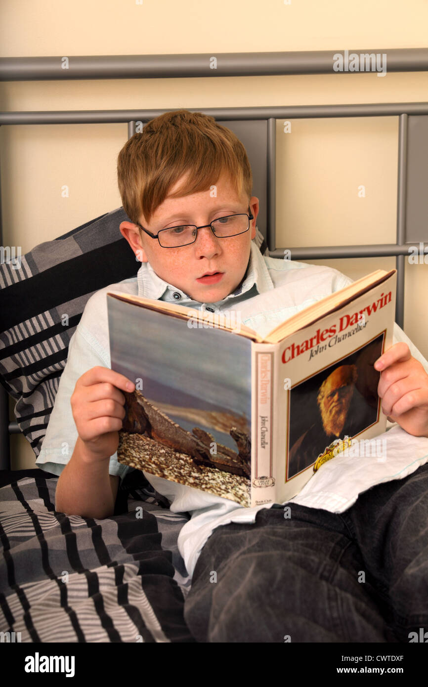 Un ragazzo di 13 anni seduto sul suo letto la lettura di un libro che parla di Charles Darwin. Il Charles Darwin libro non è mio diritto d'autore Foto Stock