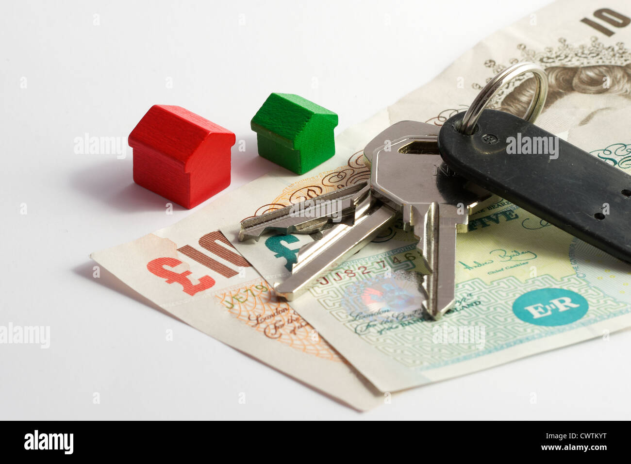 Mazzo di chiavi giacente sulla valuta britannica lungo con una rossa e una verde casa in legno. Metafora per i costi associati alla home o Foto Stock