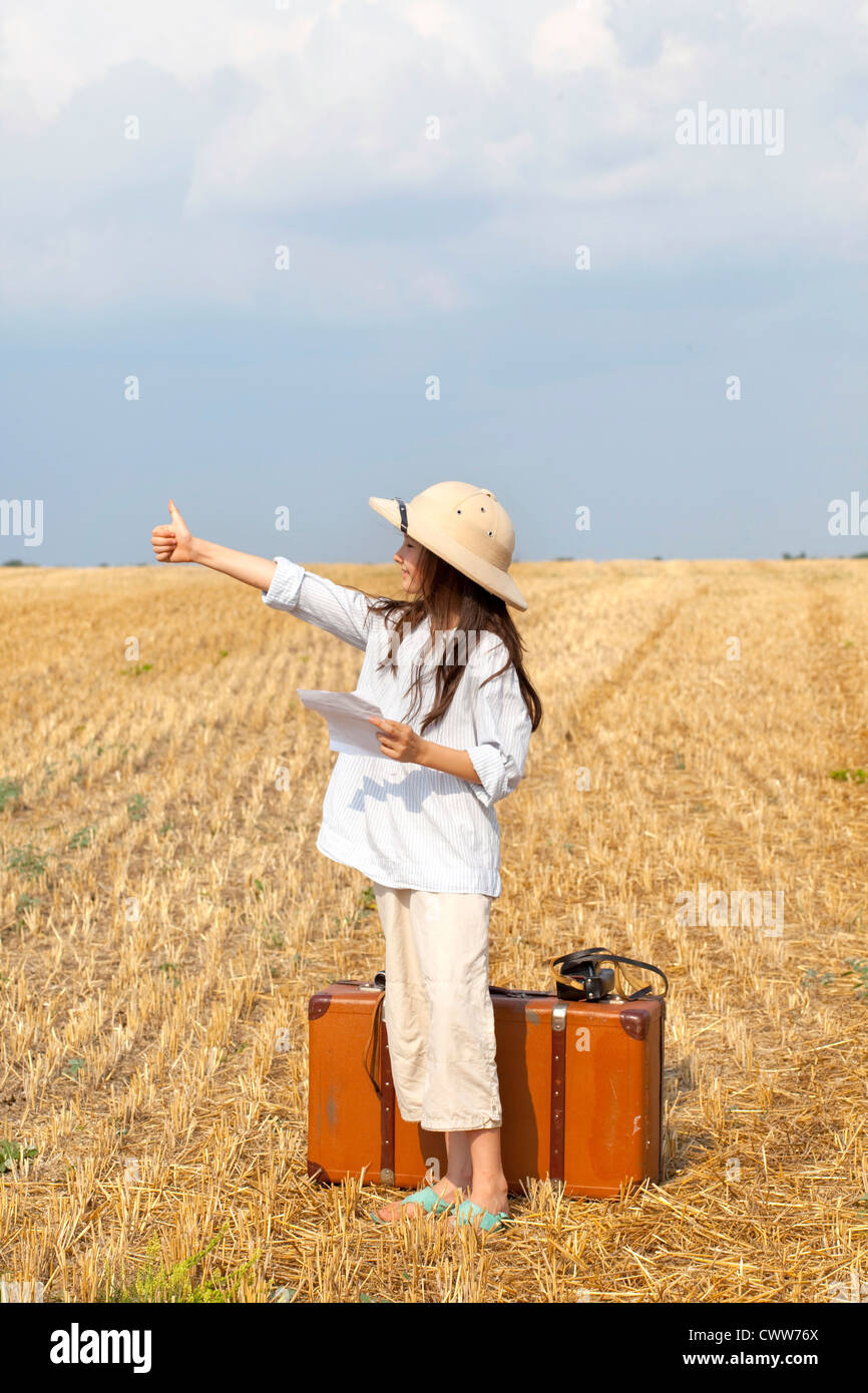 Poco 9 anni che viaggiano ragazza sul campo mietuto con il vecchio valise. Foto Stock