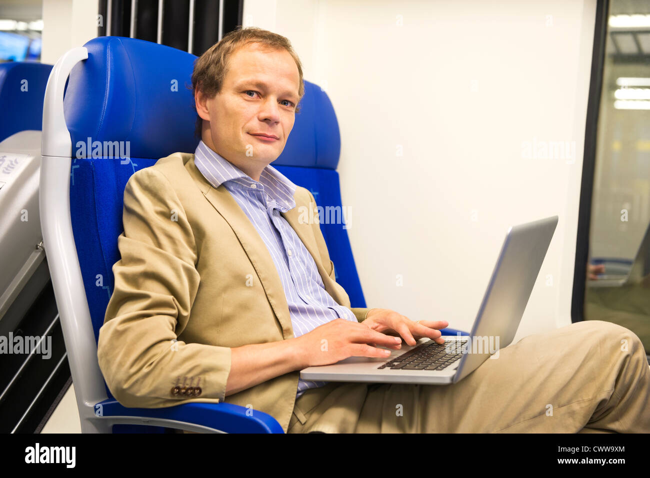 L'uomo, che indossa un abito senza cravatta è lavorare in un treno, guardando verso l'alto dal suo computer portatile Foto Stock