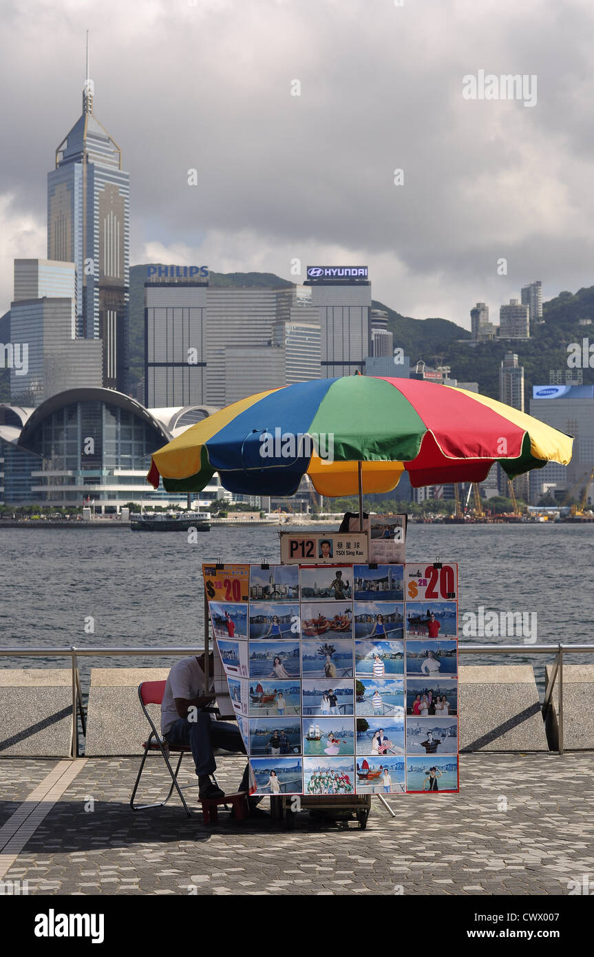 Ritrattista che esibisce le foto sotto ombrellone con lo skyline di Hong Kong in background (Hong Kong (Cina) Foto Stock