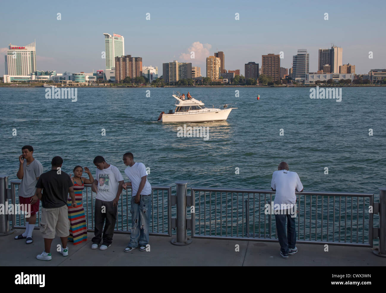 Giovani afro-americani appendere fuori lungo il Fiume Detroit come di mezza età bianchi crociera su una barca di potenza nelle vicinanze Foto Stock