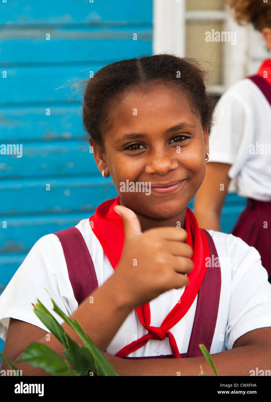 Felice e cordiale schoolgirl in uniforme scolastica dando il pollice in alto segno di Santiago di Cuba - Foto Stock
