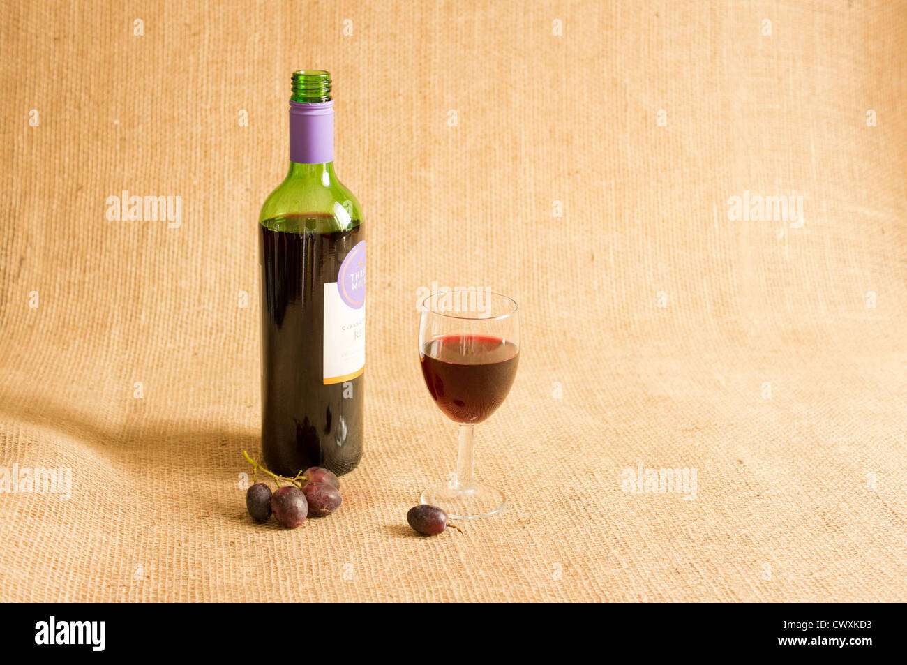 Ha aperto una bottiglia di vino rosso con un bicchiere di vino mezzo riempito con uve a bacca rossa su uno sfondo di Hesse. Foto Stock