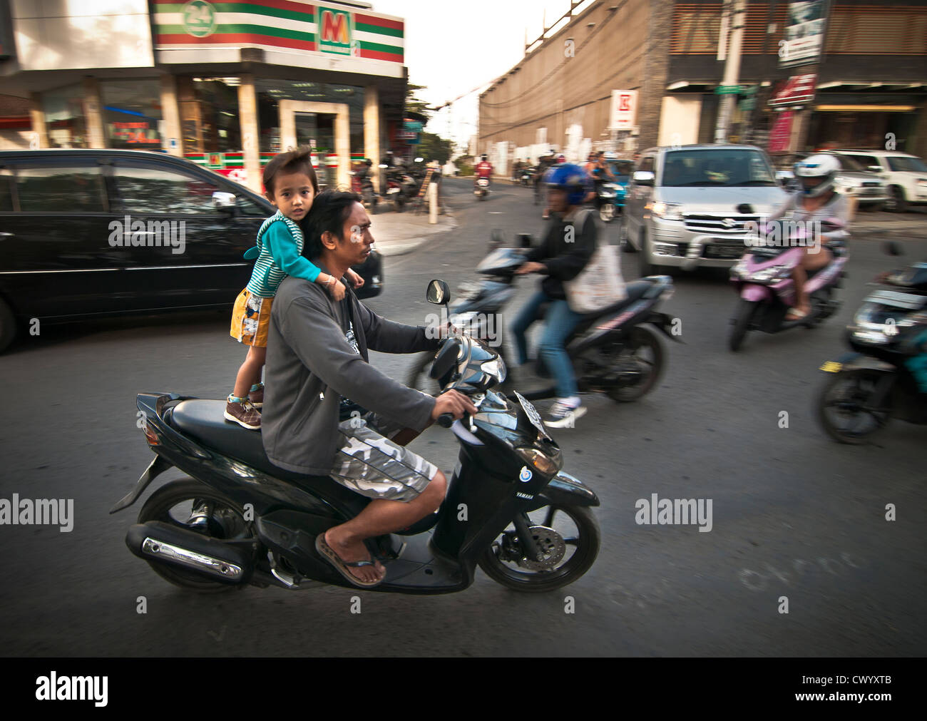Bambino sulla schiena di un ciclomotore in Legian la strada principale di Legian, meridionale di Bali, Indonesia. Foto Stock