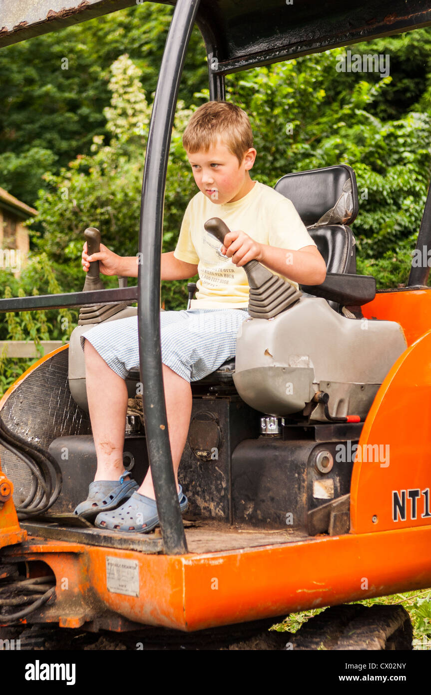 Un 8 anno vecchio ragazzo alla guida di un mini escavatore in un villaggio di fete nel Regno Unito Foto Stock