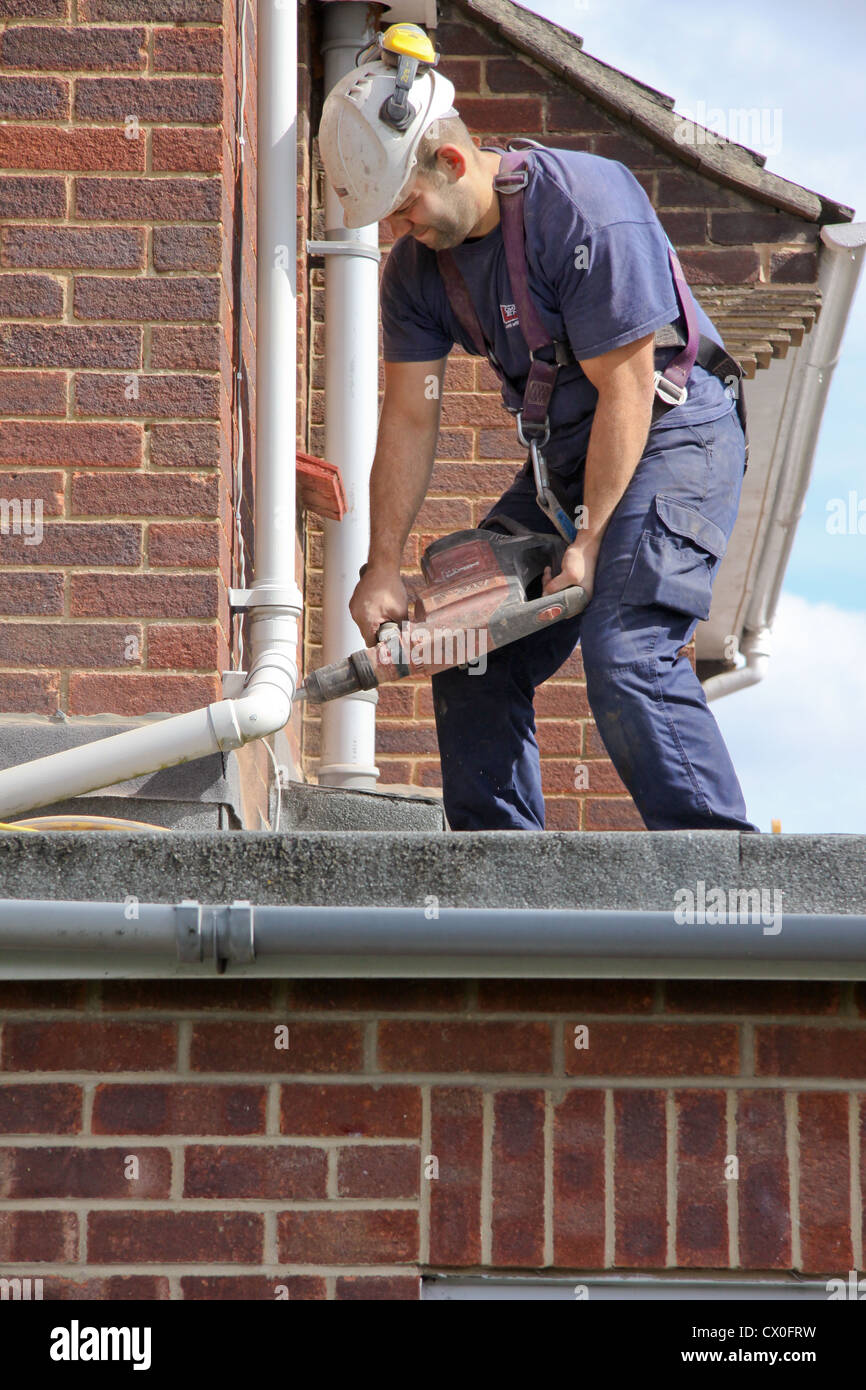 Workman perforazione di fori in una casa suburbana a parete in preparazione per la parete di cavità di isolamento Foto Stock