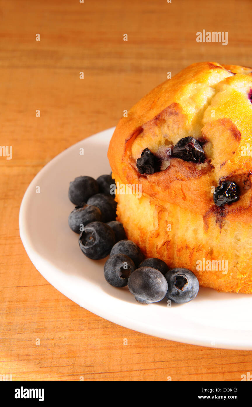 Primo piano di un muffin ai mirtilli e bacche allentato su una piastra bianca su una tavola in legno rustico. Foto Stock