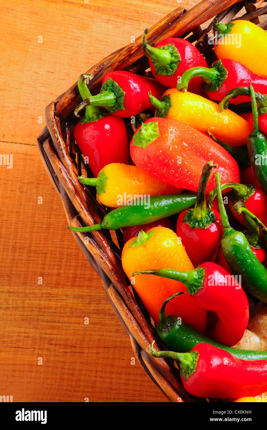 Primo piano di un assortimento di peperoni e peperoncini rossi in un cesto di vimini su una tavola in legno rustico. Foto Stock