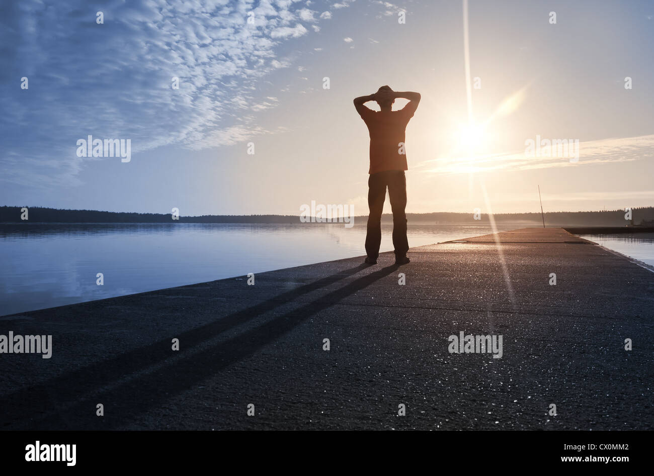 Un uomo si erge sul molo di cemento con protagonista al sole al mattino Foto Stock