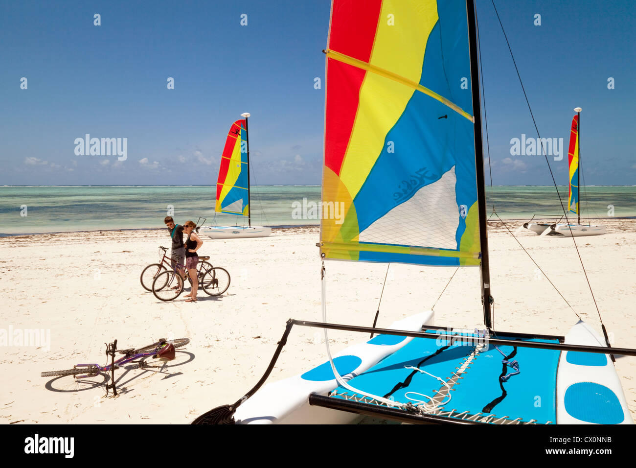 I turisti in bicicletta sulla spiaggia al centro di sport acquatici, brezze Hotel, Bjewuu, Zanzibar africa Foto Stock