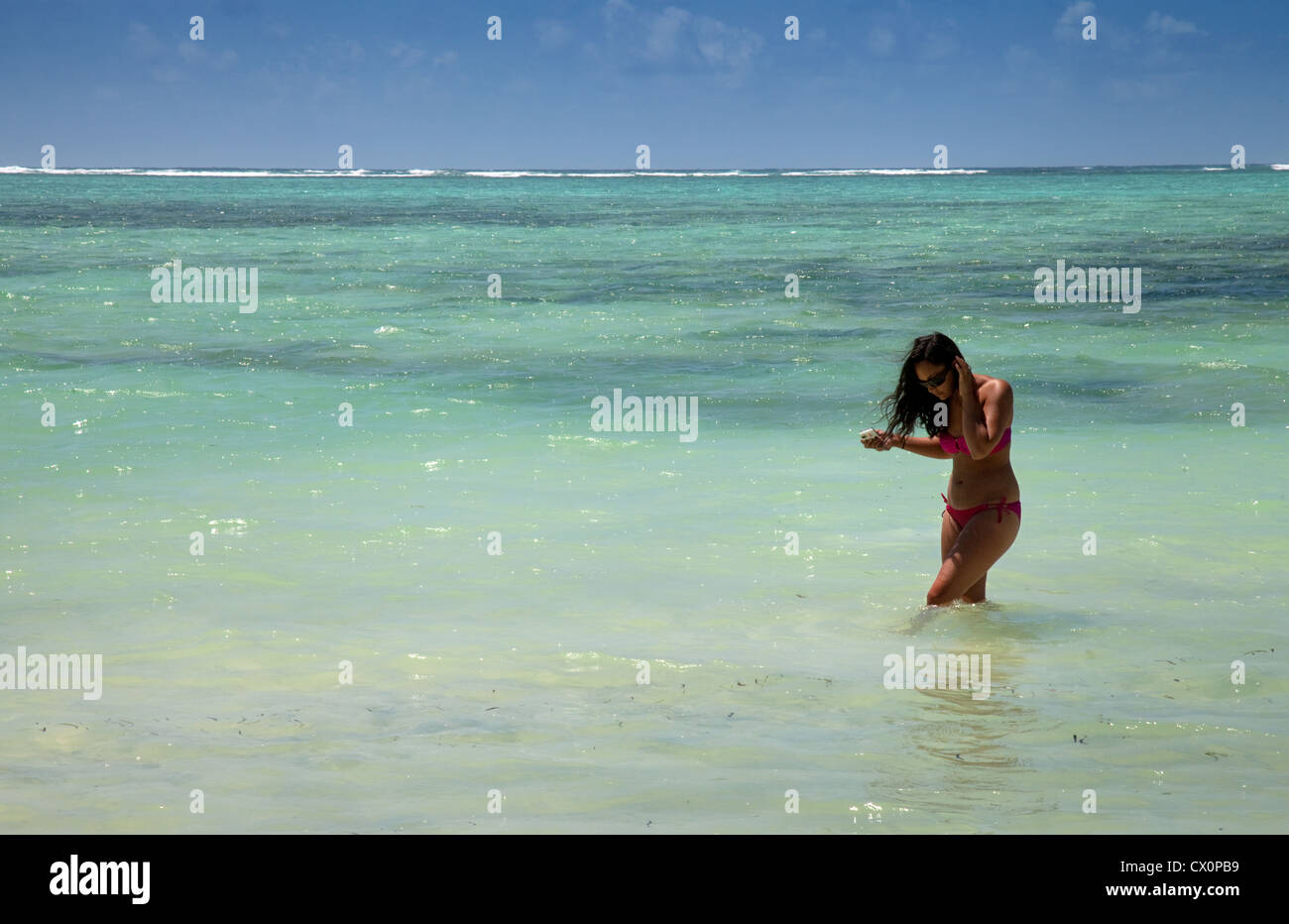 Giovane donna in piedi in acqua per una vacanza, l'Oceano Indiano a Bwejuu beach, Zanzibar Tanzania Africa Foto Stock